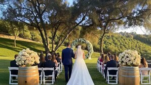 A wedding ceremony with a bride in a white dress, a groom in a suit, and guests seated on white chairs.