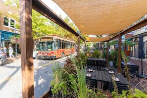 Une vue de rue avec un autobus, un espace de sièges extérieur et des bâtiments.