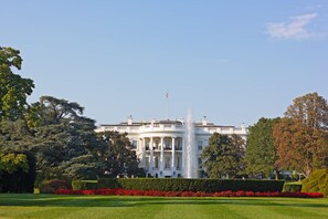 Un grand bâtiment blanc, doté d’une fontaine centrale, entouré de pelouses et d’arbres parfaitement entretenus.