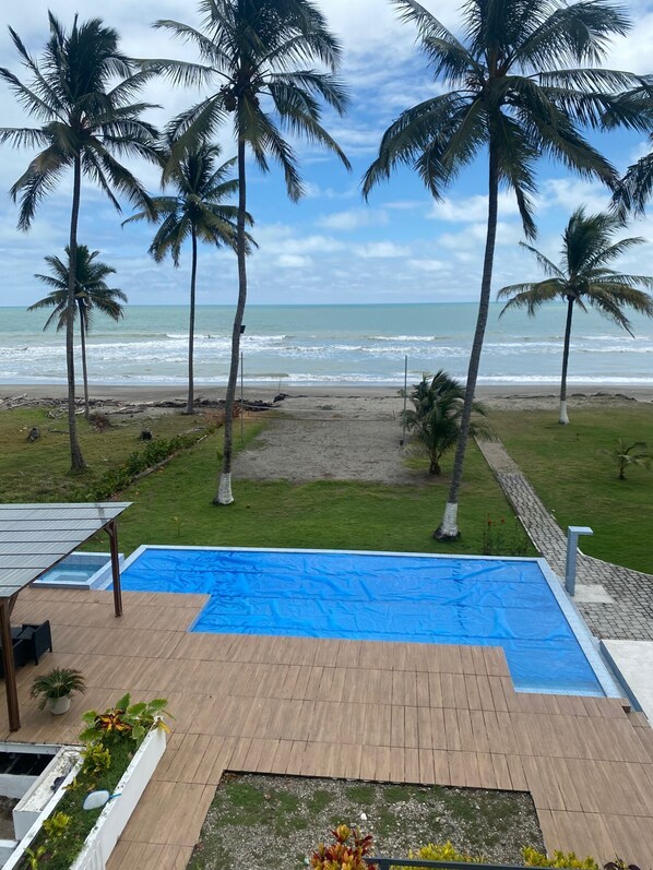 A pool area with a view of the ocean, surrounded by palm trees and a grassy lawn.