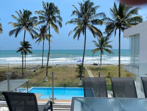 A poolside view with a clear ocean view, palm trees, and a beach with a small structure.