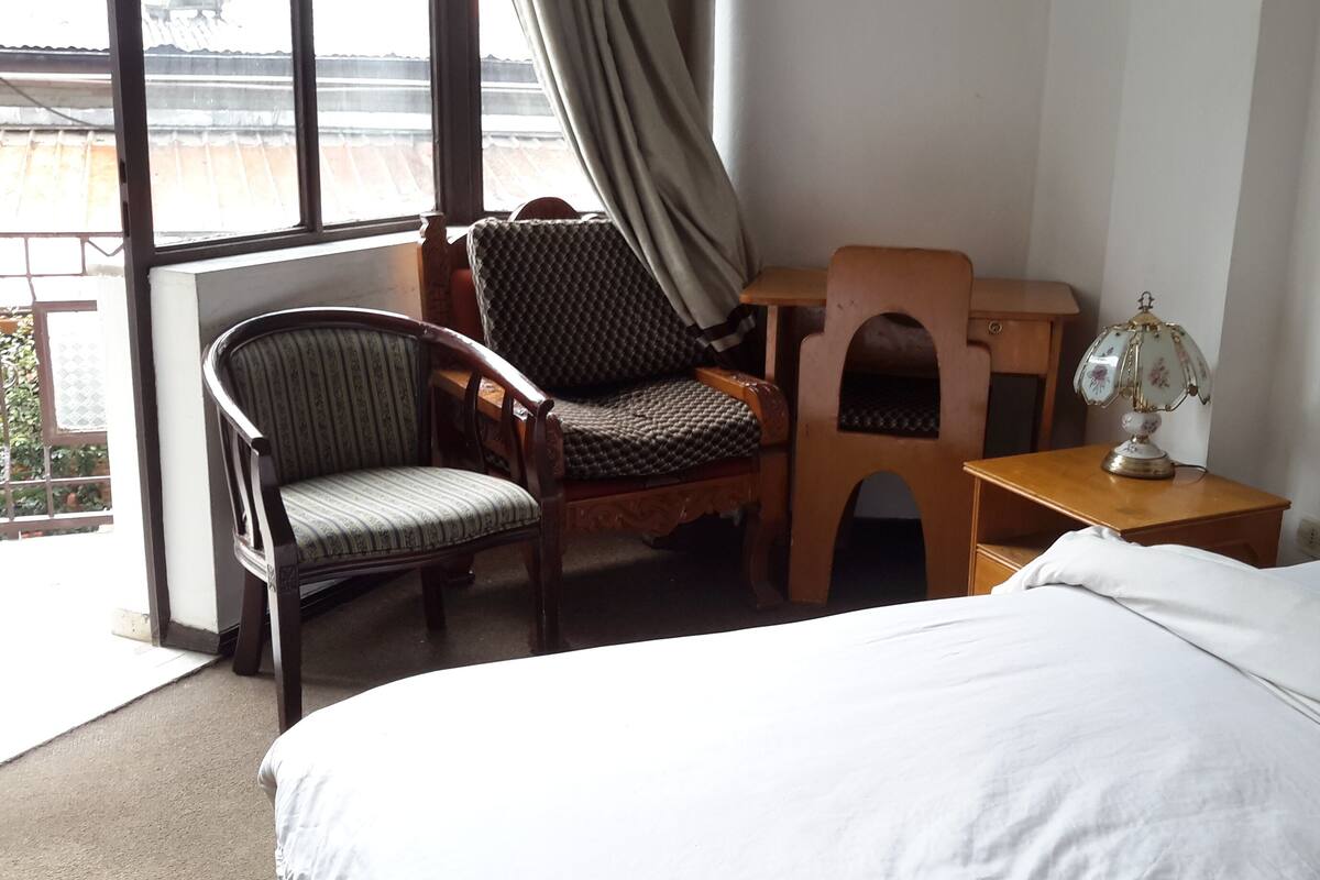 A hotel room with a bed, a desk, a chair, and a lamp.