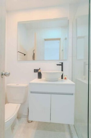 Een moderne badkamer met een witte wastafel, een spiegel erboven en een toilet aan de linkerkant.