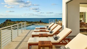 A poolside area with lounge chairs and a view of the ocean.