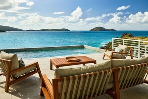 Ein Poolbereich mit Holzmöbeln und Blick aufs Meer.
