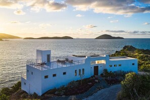 A modern white building with a rooftop terrace overlooking a calm sea and distant islands. - NEW Villa Arpeggio Luxury Oceanfront (Northside)