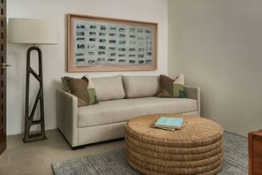 Ein Wohnzimmer mit einer Couch, einem runden Hocker, einer Stehlampe und einem abstrakten Gemälde in einem Rahmen.