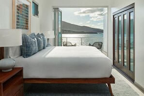 A bedroom with a large bed, a nightstand, a lamp, and a view of the sea through a sliding door. - NEW Villa Arpeggio Luxury Oceanfront (Northside)