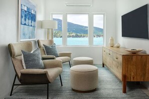 Een moderne woonkamer met een bank, twee voetenbankjes, een bijzettafeltje en een televisie.