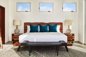 Un dormitorio ordenado con una cama grande, dos mesitas de noche con lámparas y tres ventanas en la pared.