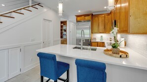 A modern kitchen with a central island, wooden cabinets, stainless steel appliances, and blue bar stools. - SOUTHERN CROSS: 3 BR, 3.5 BA home in Old Town Key West with Private Pool & AC! (Key West)
