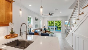 A modern kitchen with a central island, a dining area with a sofa, and a view of a tropical garden through large sliding doors. - SOUTHERN CROSS: 3 BR, 3.5 BA home in Old Town Key West with Private Pool & AC! (Key West)