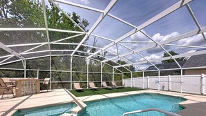 Una piscina exterior techada con sillones de descanso y una zona de barbacoa.