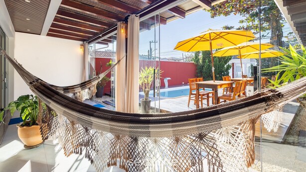A hammock in a modern room with a glass wall, a pool, and outdoor furniture.