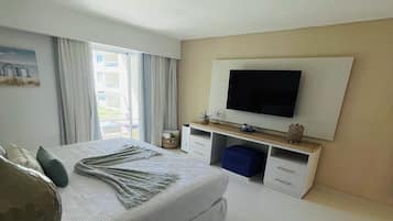 A modern hotel bedroom with a large bed, a flat-screen TV mounted on the wall, and a balcony with curtains.
