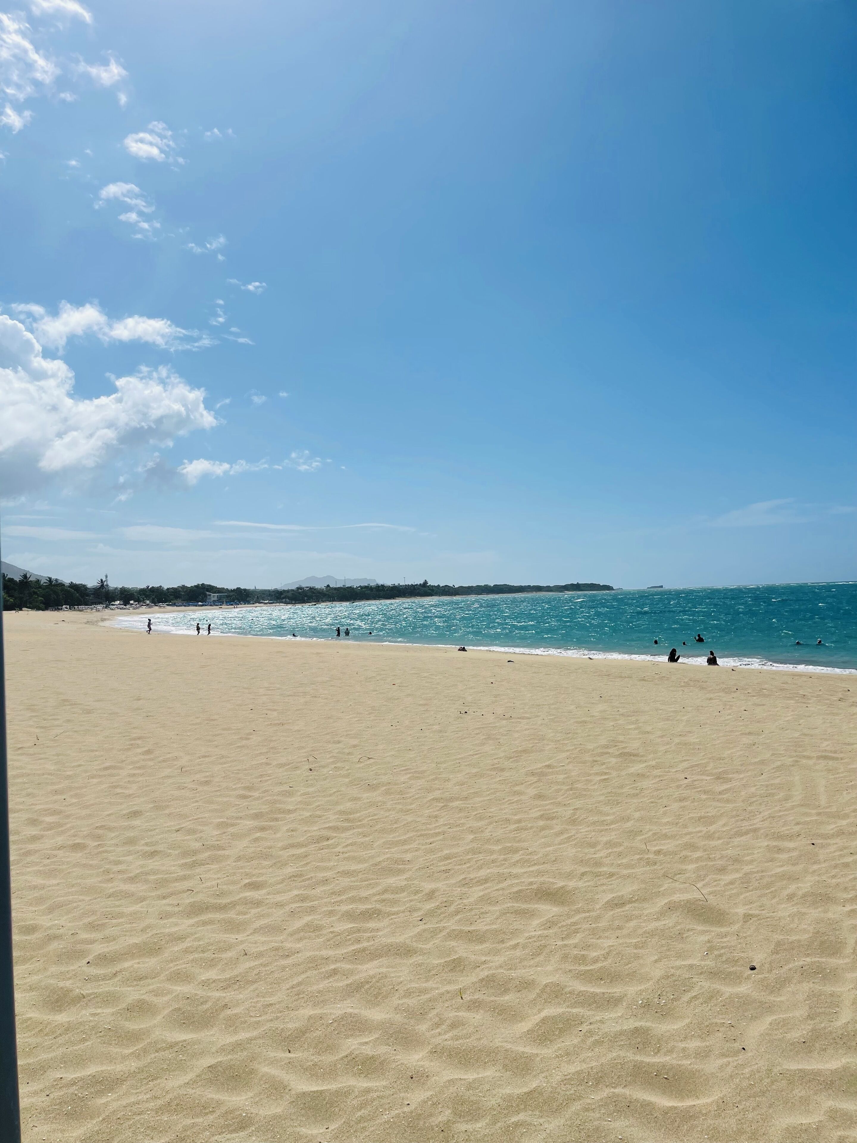 A wide sandy beach with a clear blue sky and calm sea.