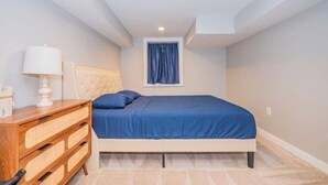 Une chambre à coucher avec un lit, une commode en bois, une lampe et une fenêtre avec des rideaux.
