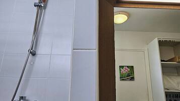Um banheiro com chuveiro, uma prateleira de madeira com uma toalha e um espelho refletindo um quarto com um quadro.