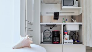 A compact kitchen with white cabinets, a microwave, a coffee maker, and a sink.