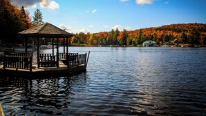 A wooden gazebo with benches on a lake, surrounded by autumn-colored trees and a clear sky. - Hemlock - Big Moose Lakeside (Eagle Bay)