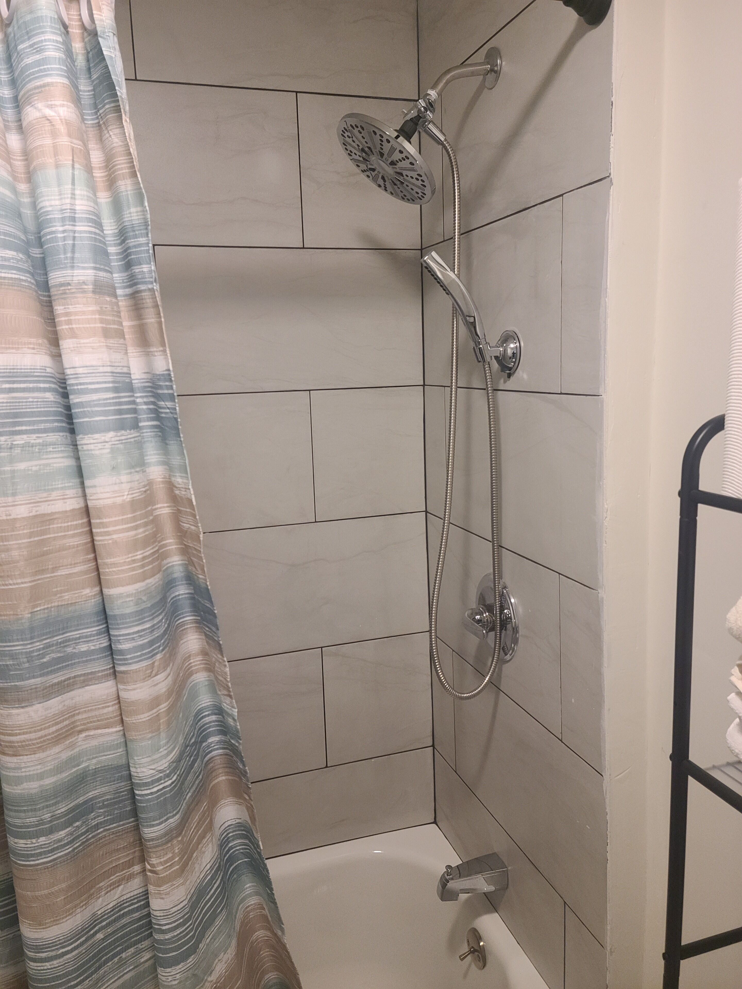 Brusebad med håndbruser og brusehose, badekar og et stribet bruseforhæng.