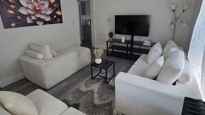 A modern living room with a sofa set, a flat-screen TV, a coffee table, and a decorative wall piece.