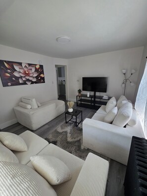 A modern living room with a sofa set, a flat-screen TV, a coffee table, and a decorative wall piece.