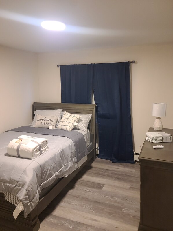 A neatly made bed with pillows and a folded blanket, a bedside table with a lamp, and a blue curtain.
