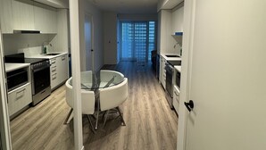 A modern kitchen with white cabinets, stainless steel appliances, and a dining area with a glass table and chairs. - Cozy Condo in Vaughan (Vaughan)
