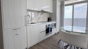 A modern kitchen with white cabinetry, a glass dining table, and a view of the ocean through large windows. - Cozy Condo in Vaughan (Vaughan)