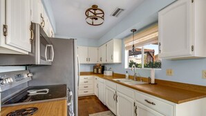 Una cocina moderna con armarios blancos, un refrigerador de acero inoxidable, encimera de madera y horno empotrado.