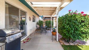 Un patio al aire libre con una parrilla, mesa, sillas y plantas en macetas.