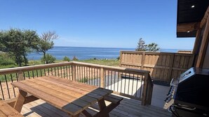 Een houten terras met een picknicktafel en barbecue, met uitzicht op een strand en de oceaan.