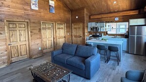 Een ruime woonkamer met houten plafond, een bank, een salontafel en een keuken op de achtergrond.