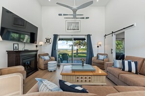 A spacious living room with a fireplace, comfortable seating, a large TV, and a view of the outdoors. - New Waterfront Luxury Cabin on Lake Winnipeg (Matlock)