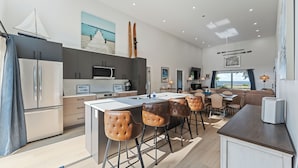 A modern kitchen with a central island, bar stools, and a dining area with a view. - New Waterfront Luxury Cabin on Lake Winnipeg (Matlock)