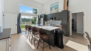 A modern kitchen with a large island, bar stools, and a view of the outdoors. - New Waterfront Luxury Cabin on Lake Winnipeg (Matlock)