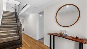 A staircase with a wooden finish, a wooden console table with decorative items, and a round mirror on the wall. - The Turnstone Retreat (Cowes)