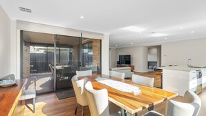 A modern kitchen with a built-in oven, a dining area with a wooden table and white chairs, and a sliding glass door leading to a patio. - The Turnstone Retreat (Cowes)