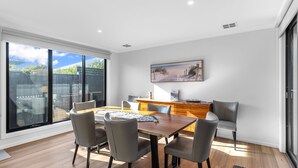 A dining area with a wooden table, six chairs, and a view of the outdoors through large sliding glass doors. - The Turnstone Retreat (Cowes)