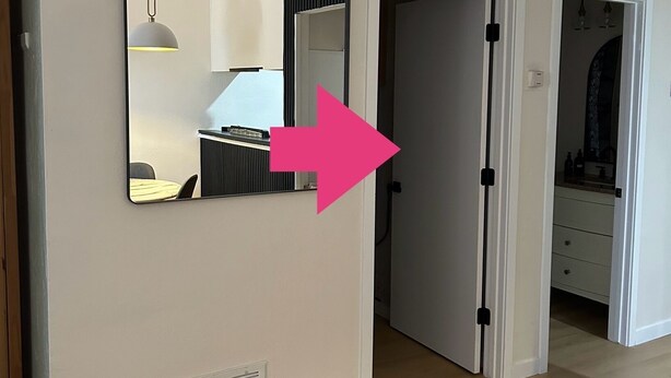 Una habitación con un espejo grande, una rejilla de ventilación y una puerta que da a otra habitación.