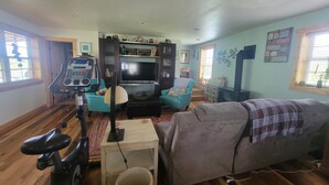 Una sala de estar con una cinta de correr, un televisor, un sofá y una mesa de comedor.