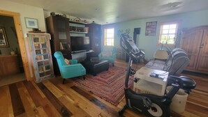 Una sala de estar con una cinta de correr, un sillón azul, un televisor y un mueble de madera.
