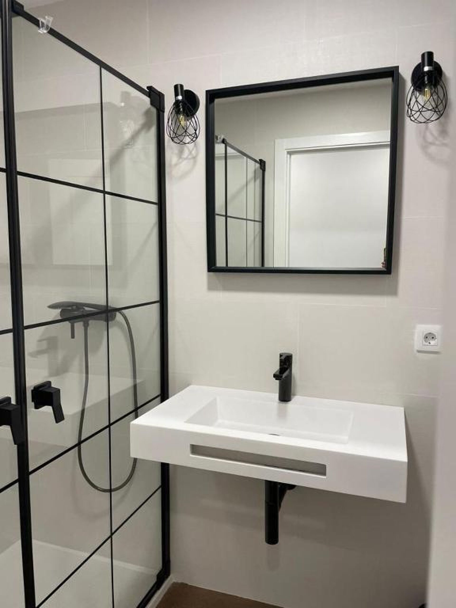 Une salle de bain moderne avec une douche à parois de verre, un lavabo blanc et un miroir avec un cadre noir.