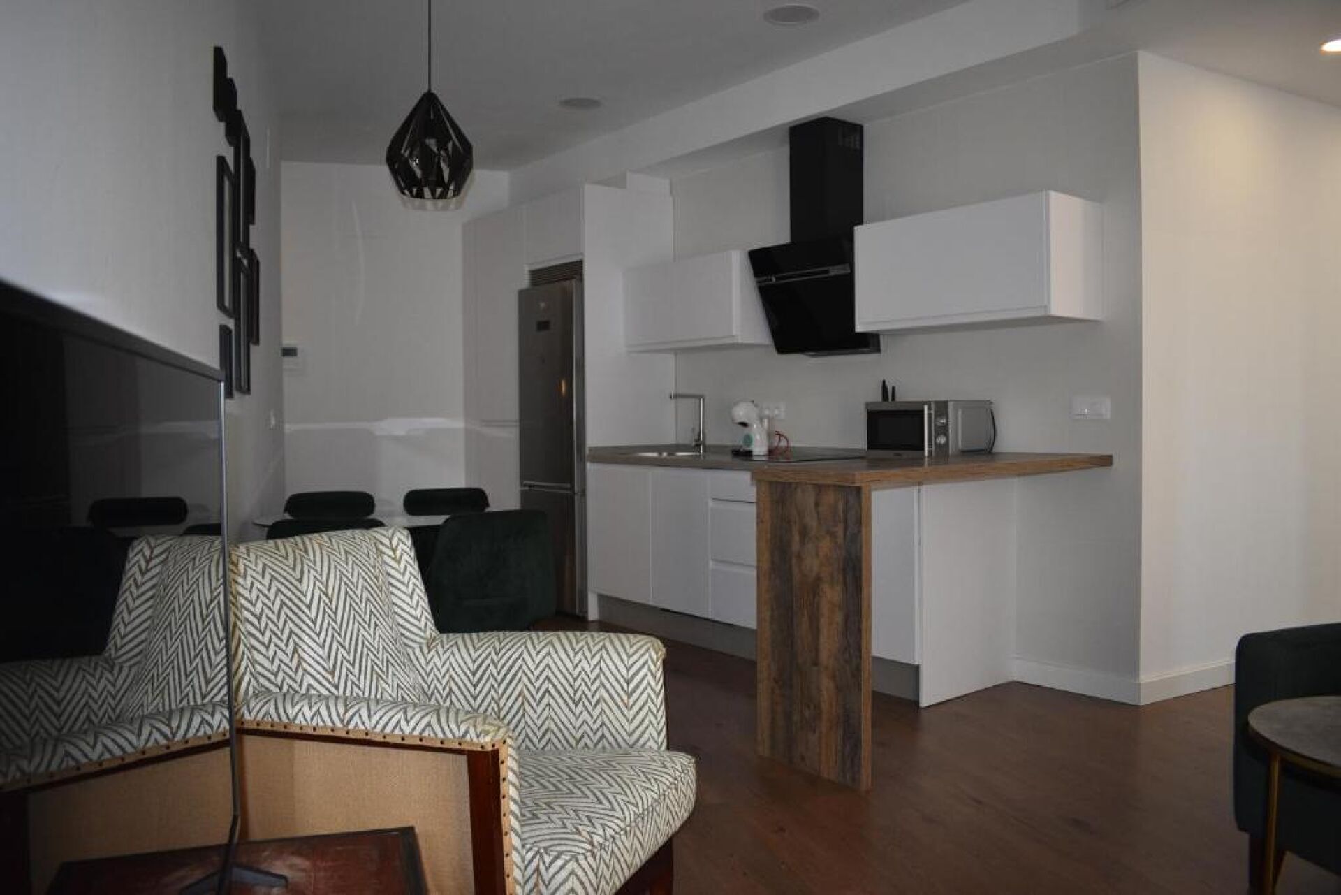 A modern living room with a sofa, a wooden coffee table, and a kitchen area with white cabinets and a microwave.