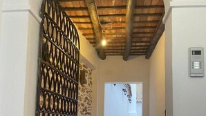 Um corredor com parede de pedra, portão de metal e teto com vigas aparentes.