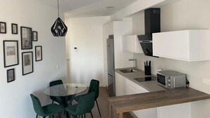 A modern kitchen with white cabinets, a microwave, and a sink. There is a dining area with a glass table and green chairs. - Mills 2 bedrooms (Constantina)