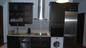 A compact kitchen with a stainless steel range hood, a built-in dishwasher, a washing machine, and dark cabinetry. - Bodeguetas 1 bedroom (Constantina)