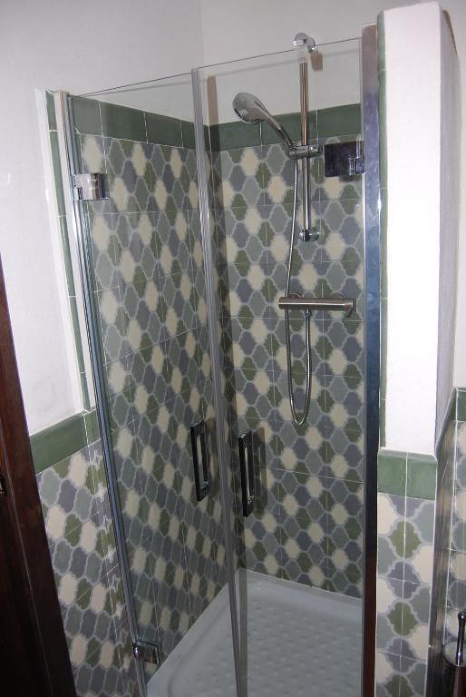 Ducha con puerta de vidrio, cabezal de ducha de mano y panel de control en la pared.