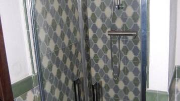 Ducha con puerta de vidrio, cabezal de ducha de mano y panel de control en la pared.